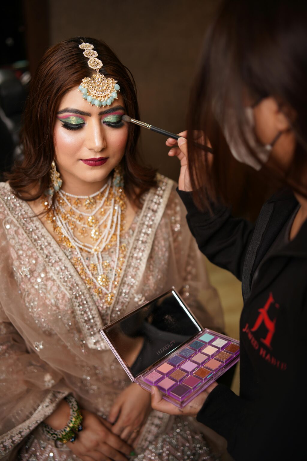 Indian bride having makeup applied with an eyeshadow palette indoors.